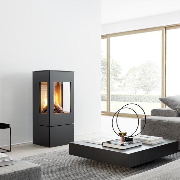 Gas-Kaminofen NEXO 100 in Schwarz mit Stahltür und zwei Seitenfenstern in einem modernen, hellen Wohnraum