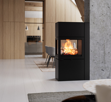 Kaminofen 600 RD in der Farbe Schwarz mit Stahltüre an einer Betonwand im modernen Wohnzimmer