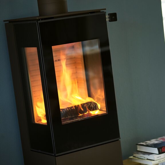 Holz-Kaminofen NEXO 120 in Schwarz mit Vollglas-Feuerraumtür und zwei Seitenfenstern, mit direktem Blick auf das brennende Feuer