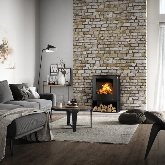 Holz-Kaminofen Q-TEE 2 C in Schwarz mit Holzfach in seiner leicht ovalen Form als Feuerstelle in einem rustikalen Landhaus