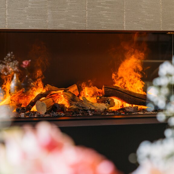 Dreiseitiger Elektrokamin e-Matrix Linear 1300/400 von Dimplex eingebaut in Steinwand mit Blumen-Dekoration