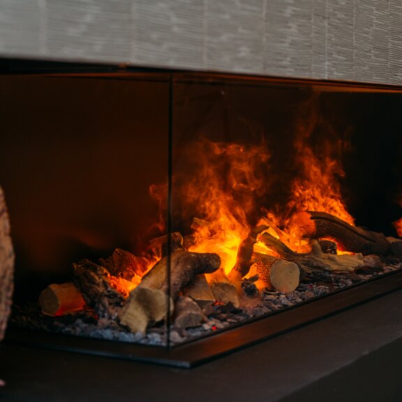 Elektrokamin e-Matrix Linear 1300/400 dreiseitig verglast von Dimplex an dunkler Steinwand eingebaut mit Kissen als Dekoration