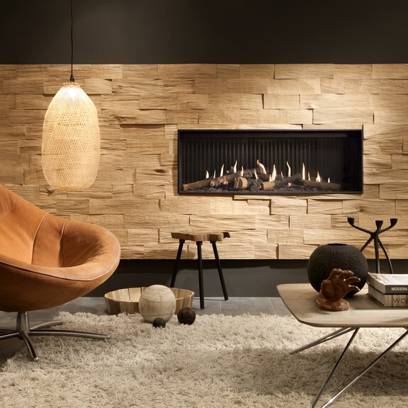 Gas-Kamin G120/41F mit Frontglas in Steinwand verbaut im Wohnzimmer mit Teppich und braunem Sessel