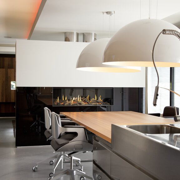 Gas-Kamin G120/41F in schwarzer Trennwand eingebaut in der Küche mit Esstisch und grossen Lampen