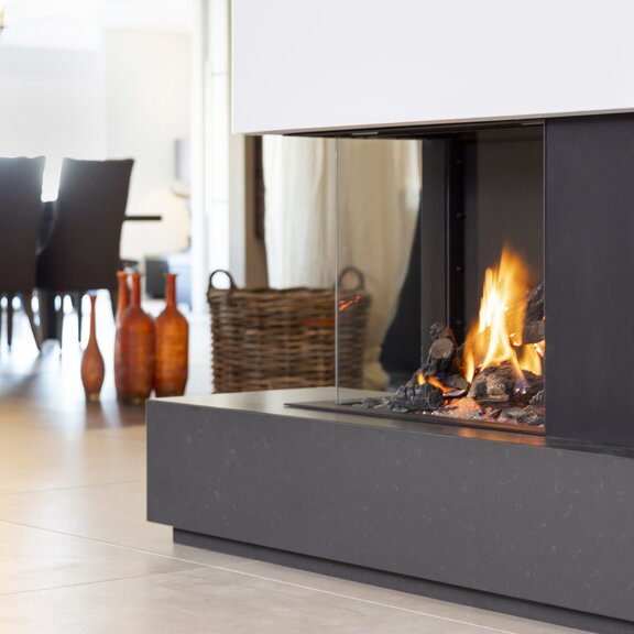 Eckversion Gas-Kamin GP65/55C auf schwarzem Sockel im Esszimmer mit Kronleuchter