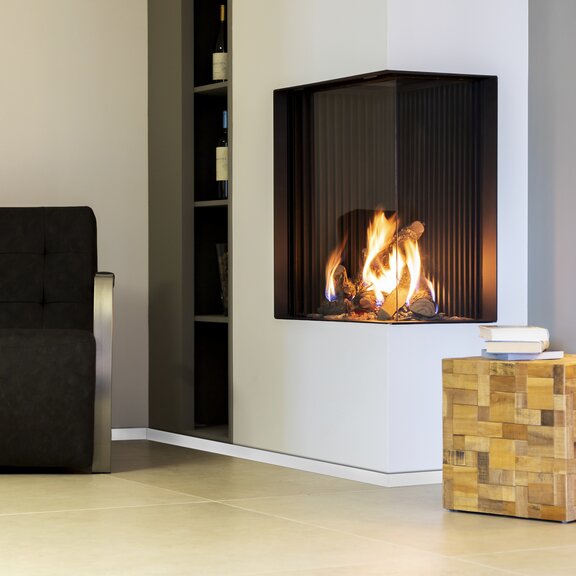 Eckvariante Gas-Kamin GP65/75C mit weisser Verkleidung im Wohnzimmer mit Regal und Sessel