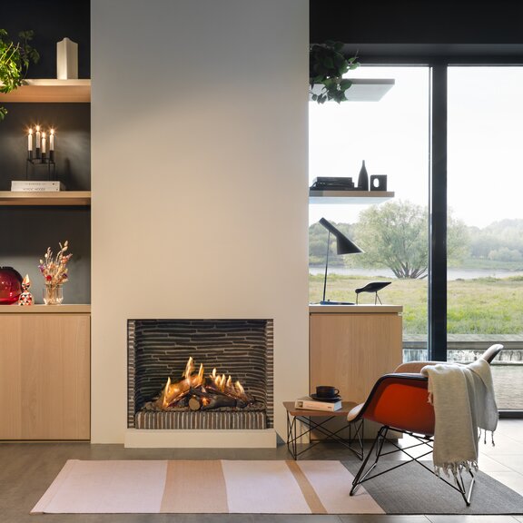 Gas-Kamin GP75/59F Front im schlichten Wohnzimmer mit grossen Fenstern und Aussicht auf grüne Landschaft und See