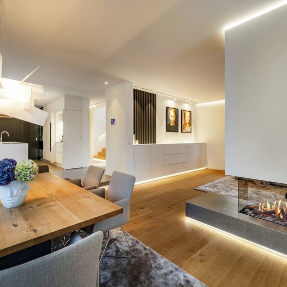 Gas-Kamin GP85/50R Raumteiler mit weisser Verkleidung im Wohnzimmer mit Küche im Hintergrund