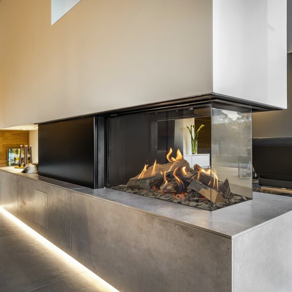 Gas-Kamin GP80/50R Raumteiler dreiseitig verglast auf Steinaufsatz und mit weisser Verkleidung im Wohnzimmer